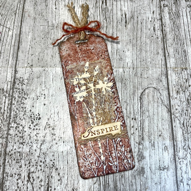 Photo of a vintage style tag with a flower die cut from a book page and the work inspire on it.